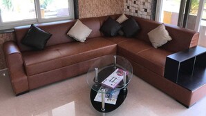 Un canapé en cuir marron avec quatre coussins, une table basse en verre avec des magazines, et un mur à motifs en arrière-plan.