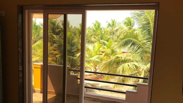 Une pièce dotée d’une grande porte-fenêtre coulissante qui donne sur un balcon offrant une vue sur des palmiers et un bâtiment jaune.