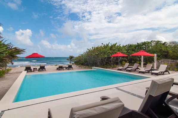 A pool with lounge chairs and umbrellas, overlooking the ocean.
