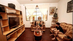 Una sala de estar con televisor, estanterías de madera, sofá, mesa de centro y ventana con cortinas.
