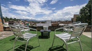 Una terraza en la azotea con dos sillas de metal y una pequeña mesa, rodeada de césped artificial verde, bajo un cielo despejado.