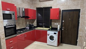 Une cuisine moderne avec des meubles rouges, un four en acier inoxydable, un lave-linge et une cuisinière noire.