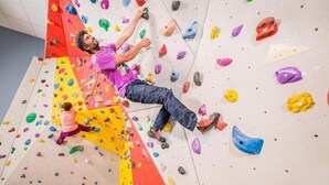 Une personne escalade un mur d’escalade intérieur aux couleurs vives, doté de différentes prises.