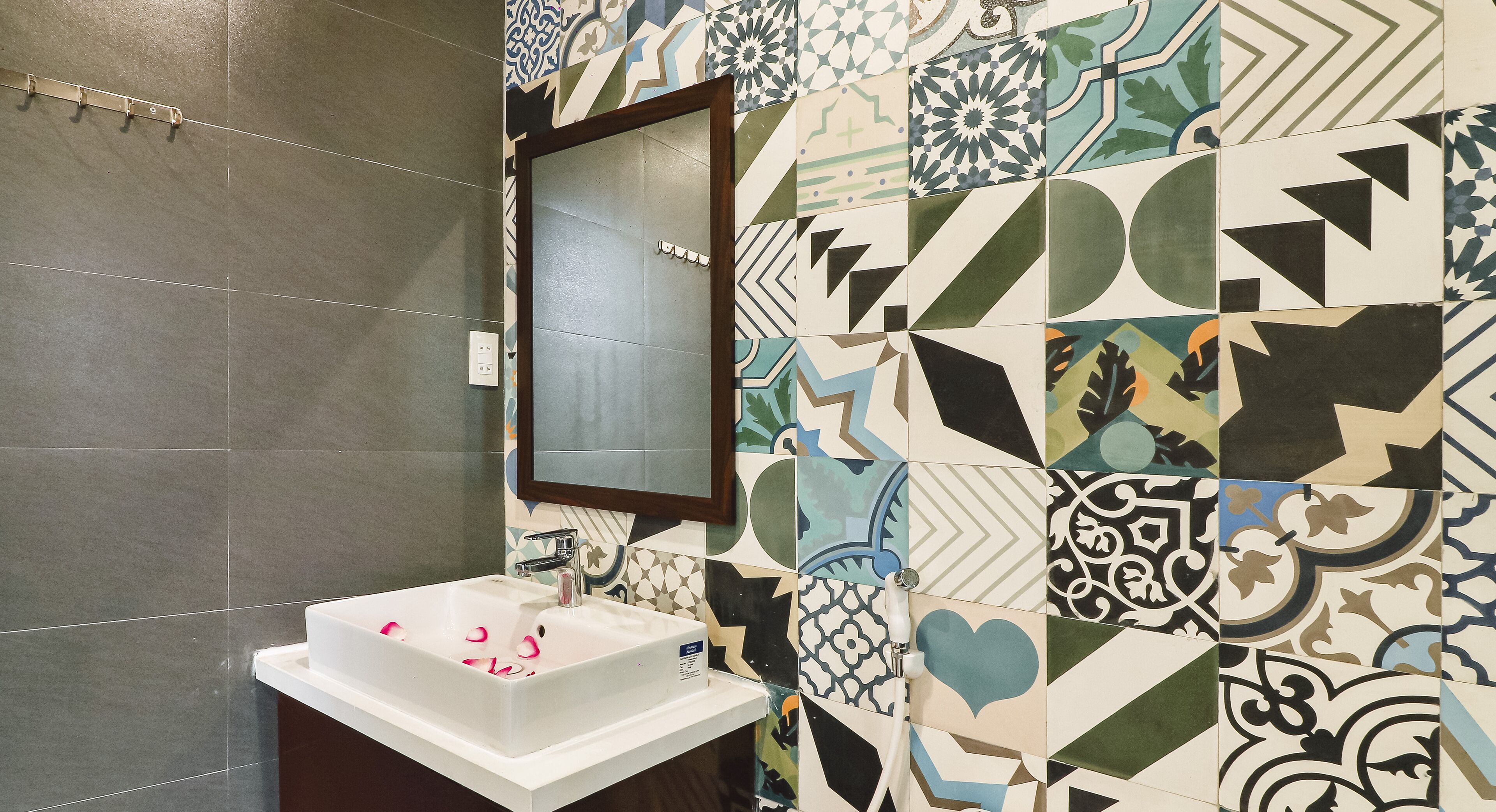 Ein Badezimmer mit weißem Waschbecken, einem Spiegel und einer gefliesten Wand mit geometrischen Mustern.