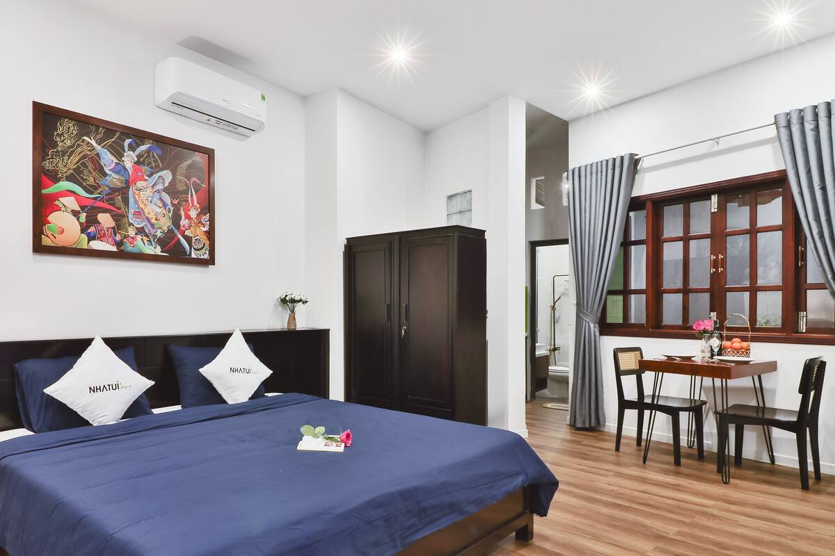A hotel room with a bed, a desk, a chair, a wardrobe, and a painting on the wall.