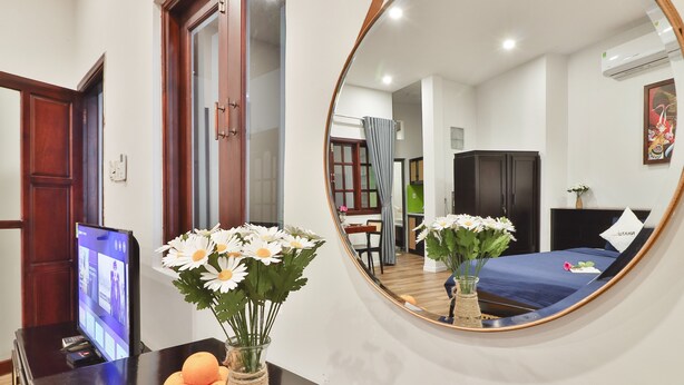 A hotel room with a bed, a desk with a computer, a mirror, and a vase with flowers.