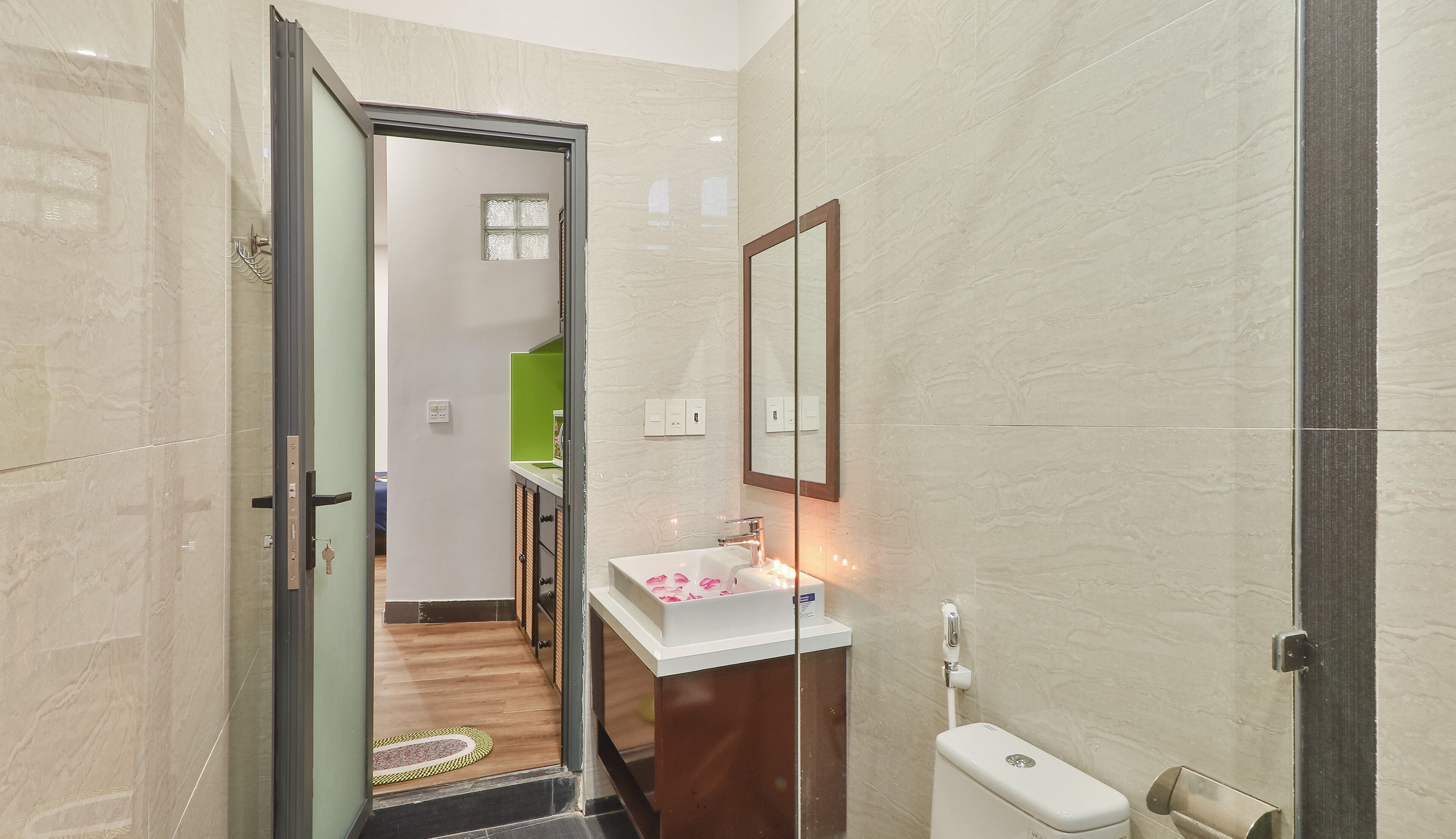 Un baño moderno con cabina de ducha de vidrio, un lavamanos blanco con un espejo encima y un inodoro.
