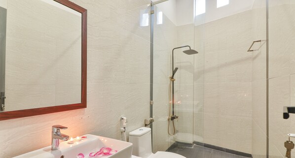Un baño moderno con cabina de ducha de vidrio, lavamanos blanco con espejo y un inodoro.