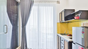 A compact kitchen with a refrigerator, a sink, and a window with curtains.