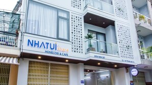 A modern building with a sign for "NHATUI Share Homestay & Cafe" and a contact number.