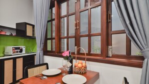 A dining area with a wooden table, two plates, a wine glass, a bottle, and a basket of oranges.
