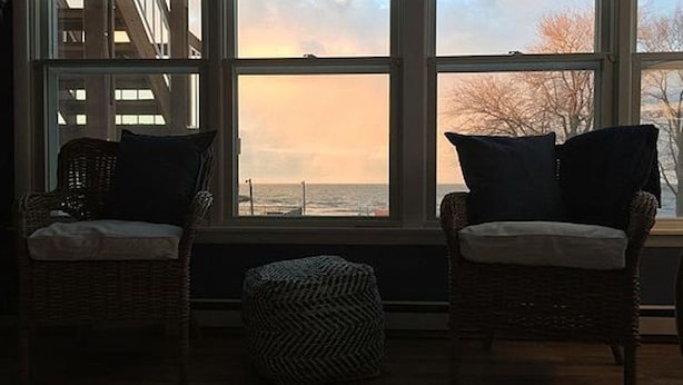 Une pièce avec deux fauteuils en osier placés face à une grande fenêtre donnant sur une étendue d’eau.