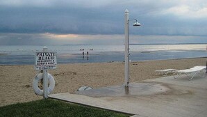 Une plage privée, avec un panneau indiquant qu’elle est réservée aux résidents et à leurs invités, une bouée de sauvetage et des chaises de plage.