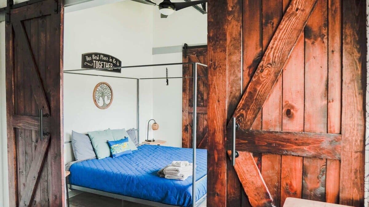 A bedroom with a bed, a wooden door, a sign on the wall, and a circular wall decoration.