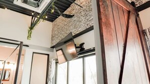 Ein Zimmer mit Backsteinwand, Holztür, Fenster und Decke mit freiliegenden Balken und hängenden Pflanzen.