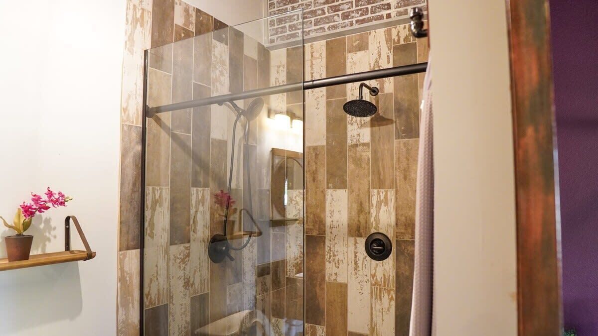 A glass-enclosed shower with a wooden tile wall, a showerhead, and a control panel.
