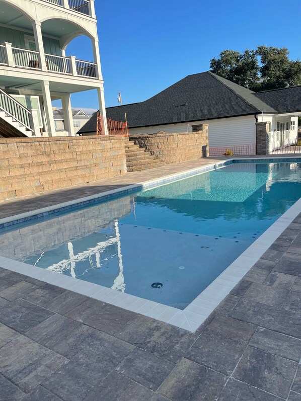 Une piscine rectangulaire bordée de pierres, un mur en briques et un immeuble à plusieurs étages avec des balcons en arrière-plan.