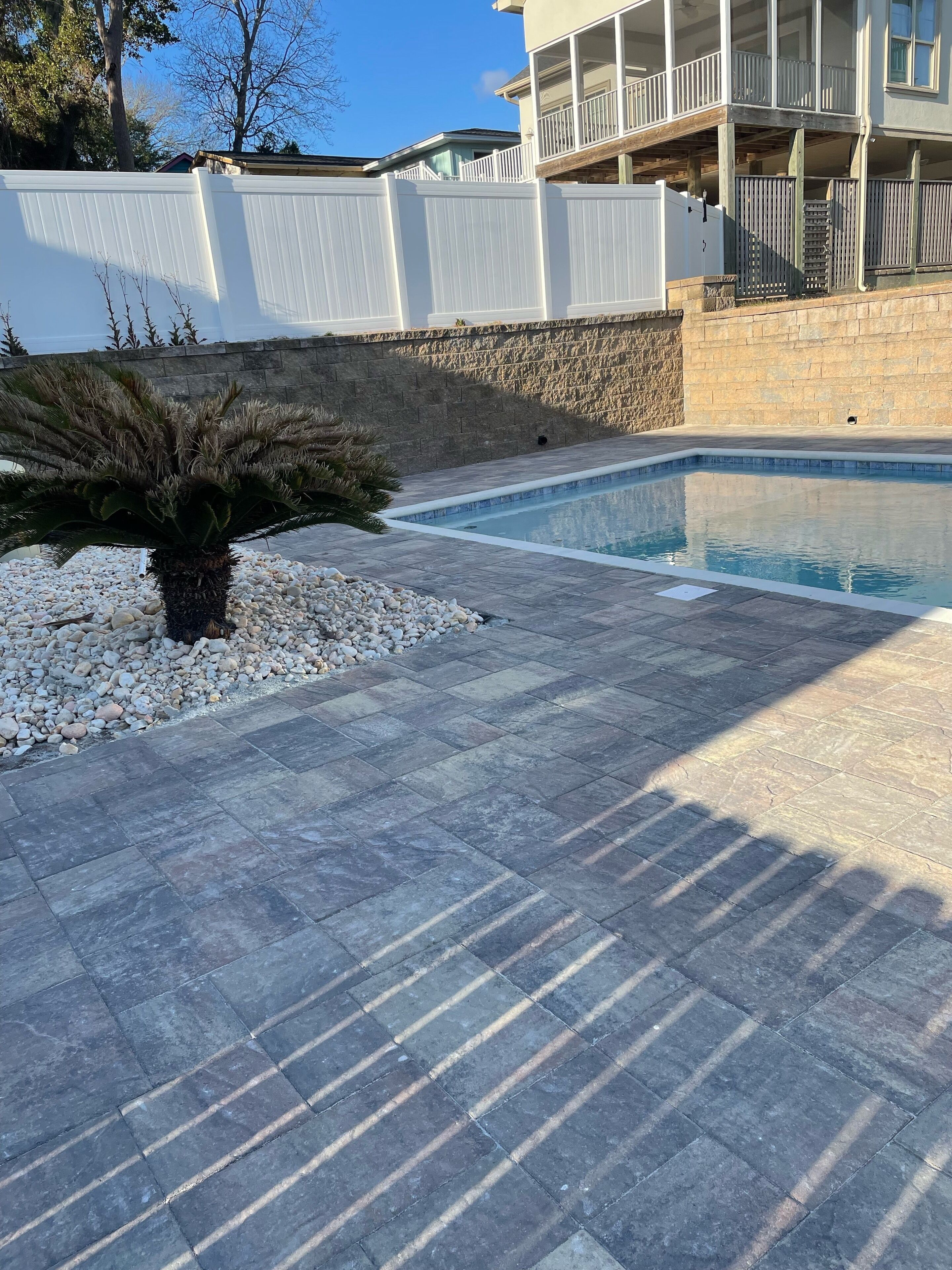 A swimming pool with a stone deck and a white fence.