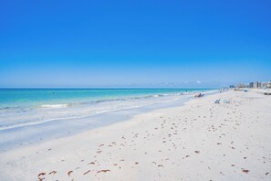Ein Strand mit blauem Himmel, sandigem Ufer und einigen Personen.