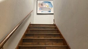 Een houten trap met een leuning, die leidt naar een kunstwerk in een lijst aan de muur.