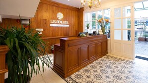 Un espace d’accueil avec un comptoir de réception en bois, un lustre et une enseigne indiquant « LE SOLEIL, hôtel-boutique ».