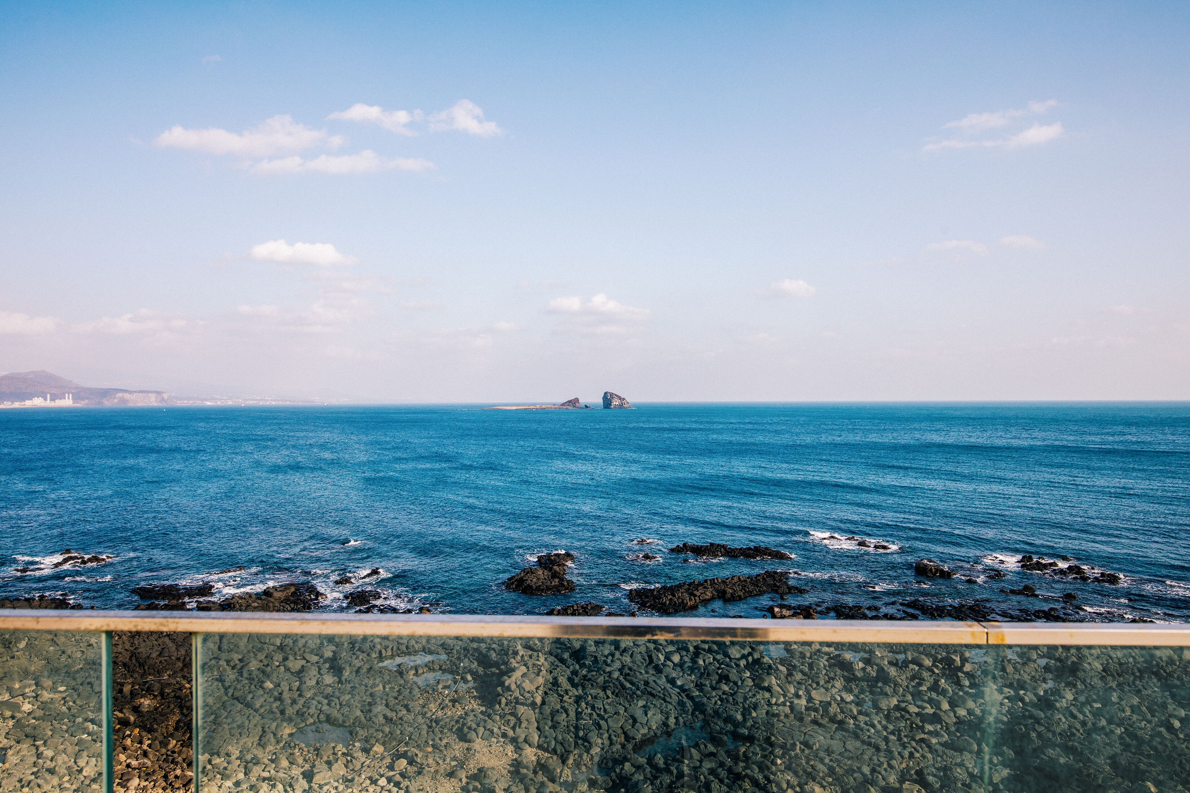 A coastal view with a rocky shoreline and a distant island.