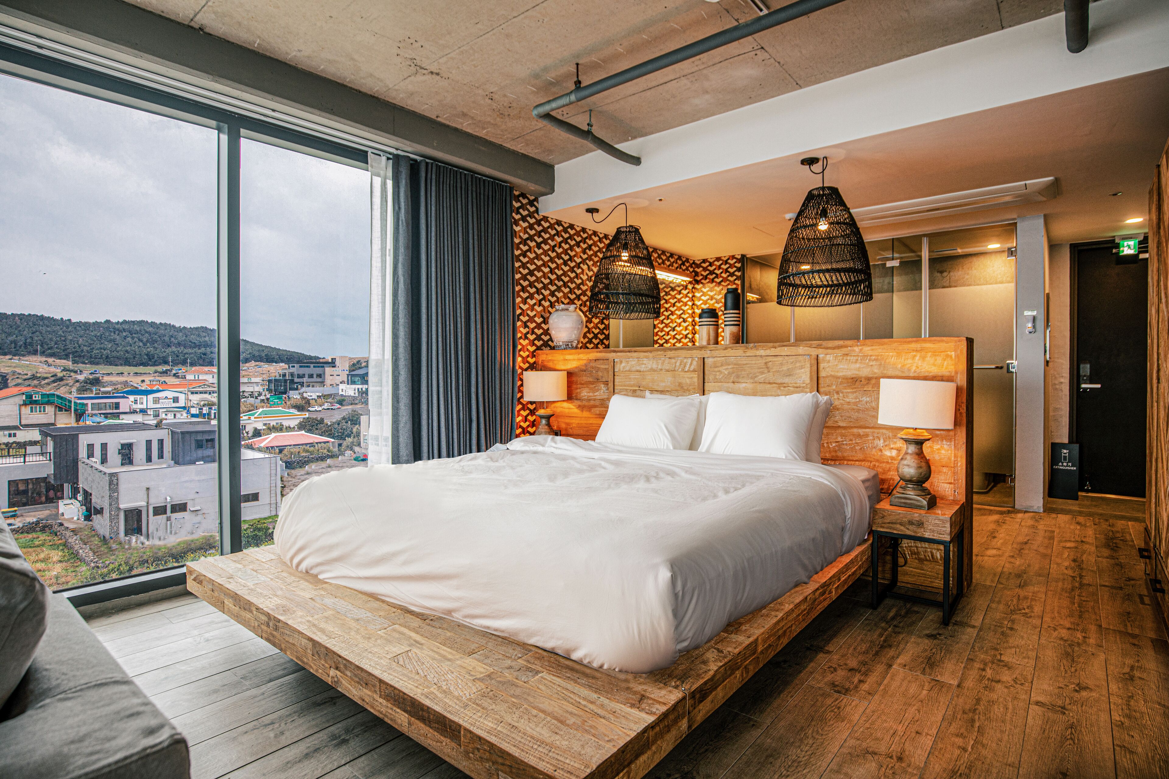 A modern hotel room with a large bed, wooden platform, city view, and stylish decor.