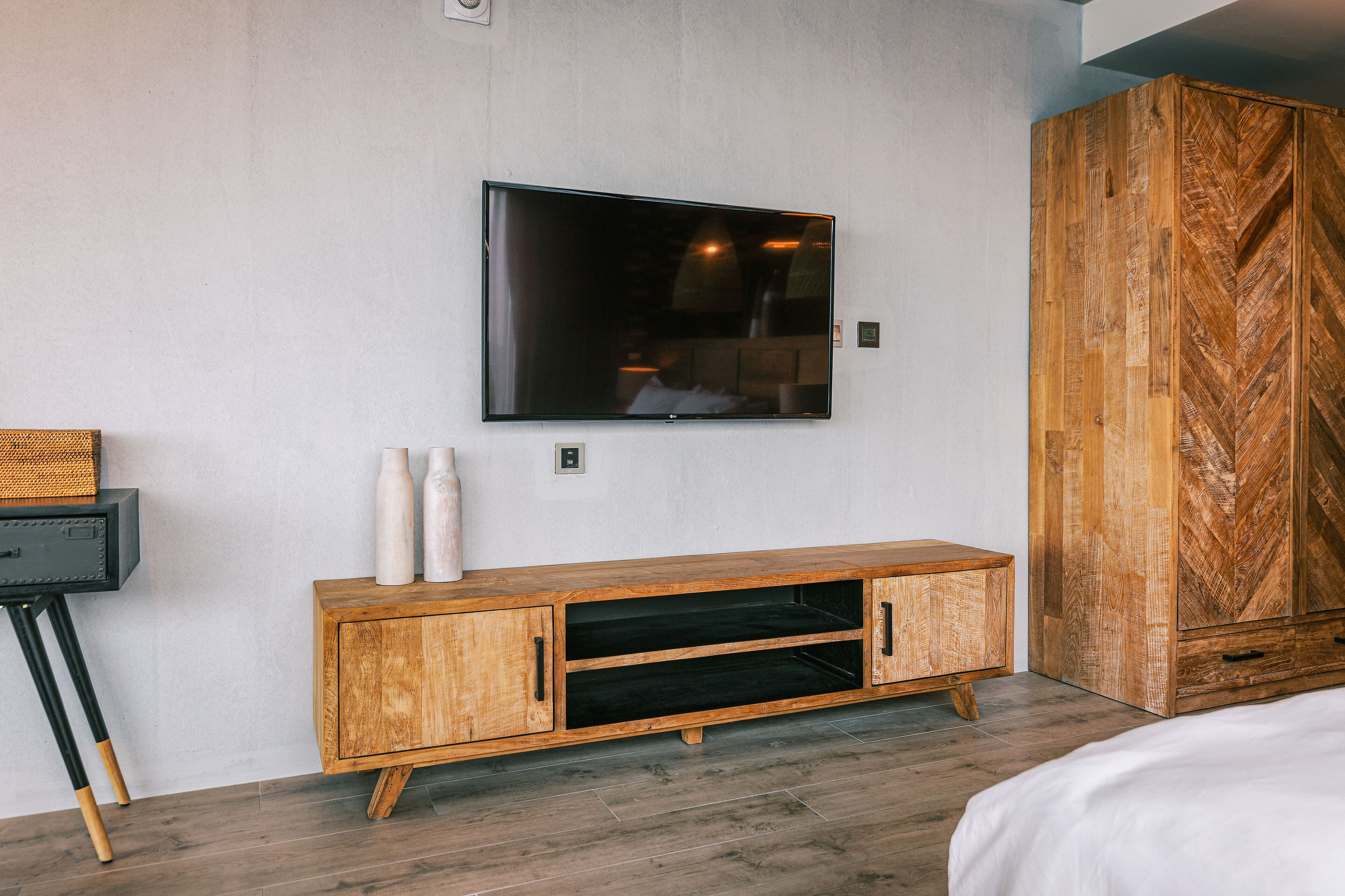 A modern bedroom with a wooden cabinet, a flat-screen TV mounted on the wall, and a large wardrobe.