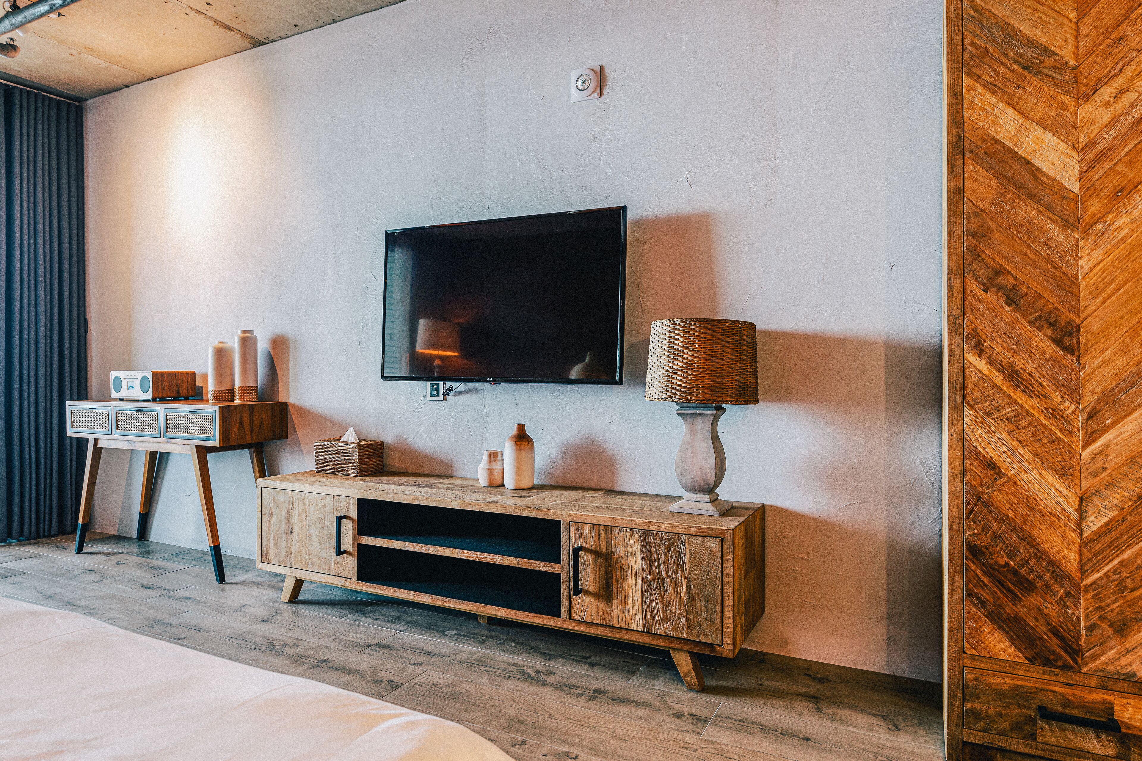 Moderni hotellihuone, jossa on puinen kaappi, litteänäyttöinen televisio ja lamppu.