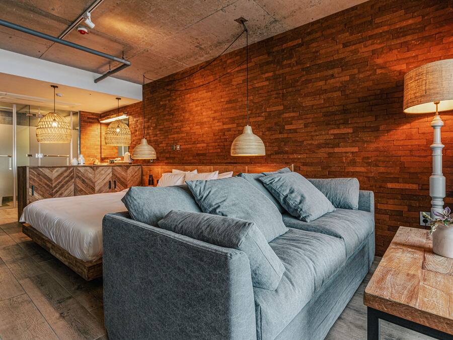 A modern hotel room with a brick wall, a grey sofa, a wooden coffee table, and pendant lighting.