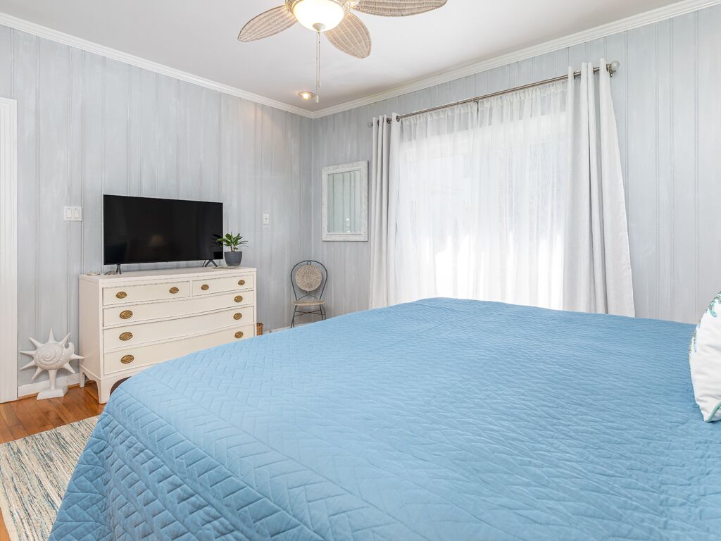 Un dormitorio con una cama grande, un aparador, un televisor y un ventilador de techo.
