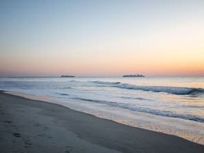 A beach with a calm sea and a distant ship.