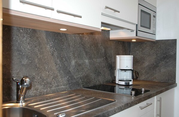 A modern kitchen with a built-in microwave, coffee maker, and stainless steel sink. - TAN 2 süd Plus Du/wc - Appartements Vilsalp (Bogen)