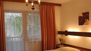 Ein Hotelzimmer mit Bett, einer Kandelaber, einem Fenster mit Vorhängen und einem Nachttisch mit Blumenvasen.
