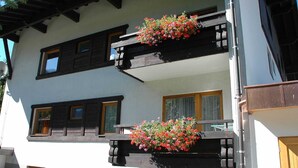 Ein zweistöckiges Gebäude mit Balkonen, Holellbögeln und Blumenkästen.