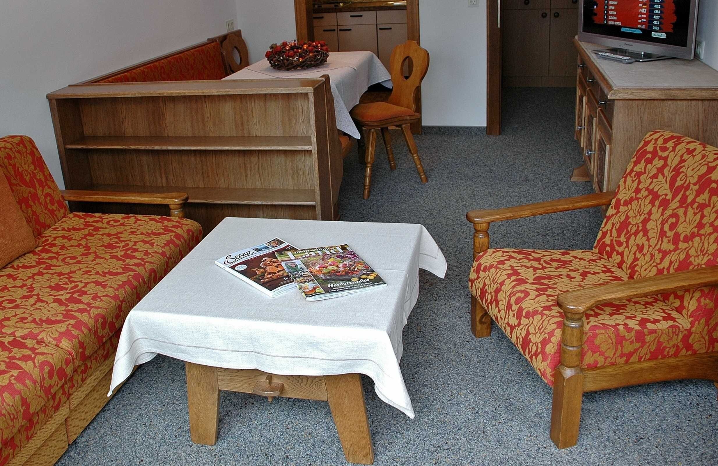 A room with a sofa, a chair, a small table with a magazine, and a television on a cabinet.