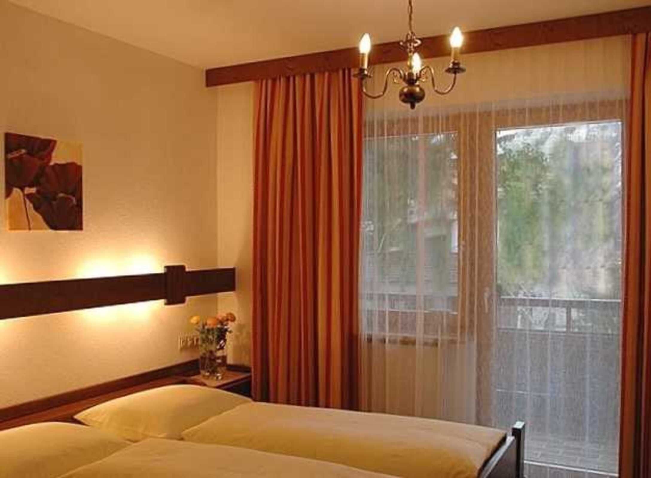 Ein Hotelzimmer mit einem Bett, einer Chandelüster, einem Gemälde und einem fenster mit Vorhängen.