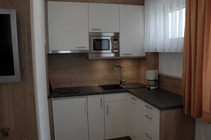 A modern kitchen with white cabinets, a stainless steel microwave, a sink, and a coffee maker.