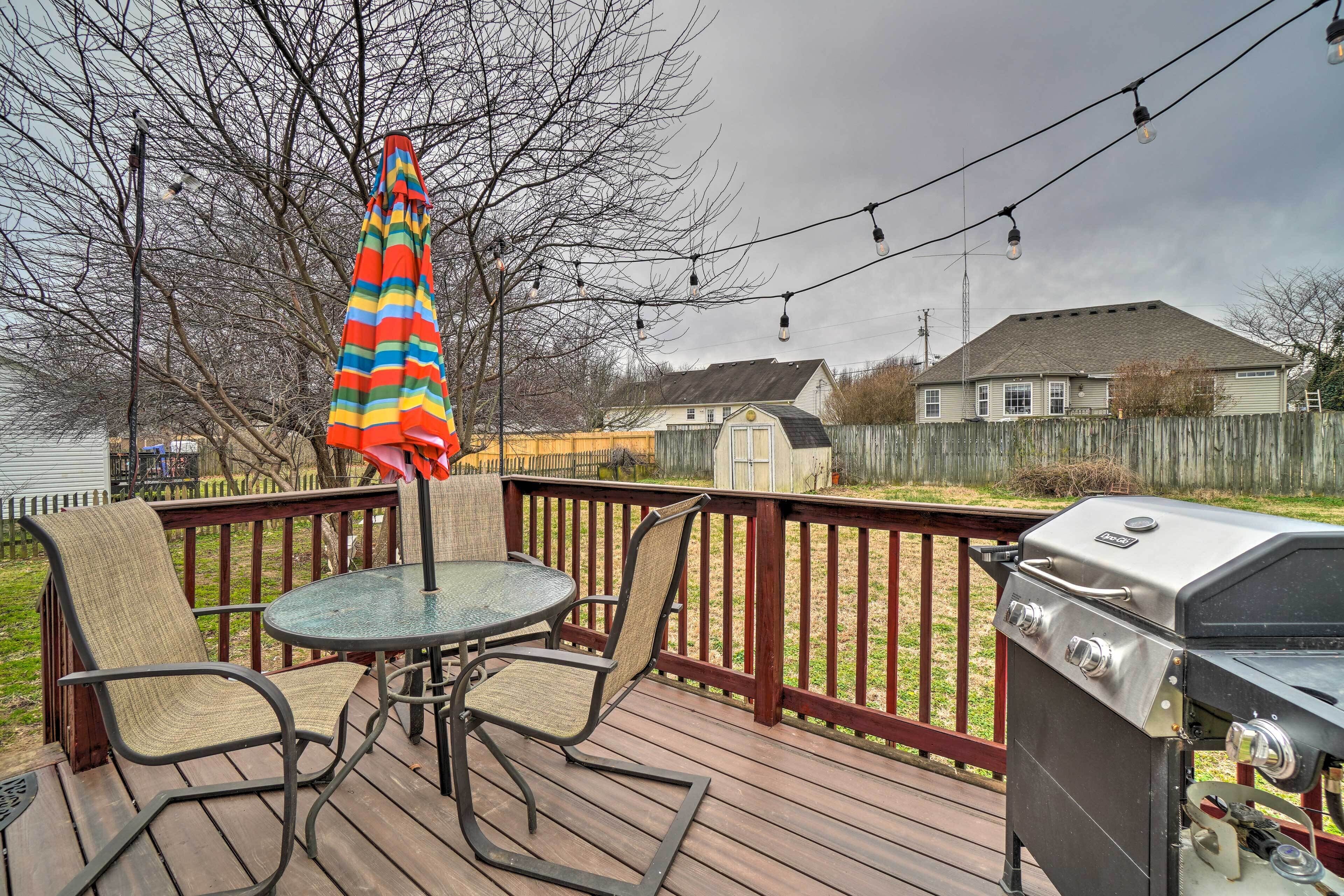 Une terrasse avec un barbecue, des chaises et un parasol.