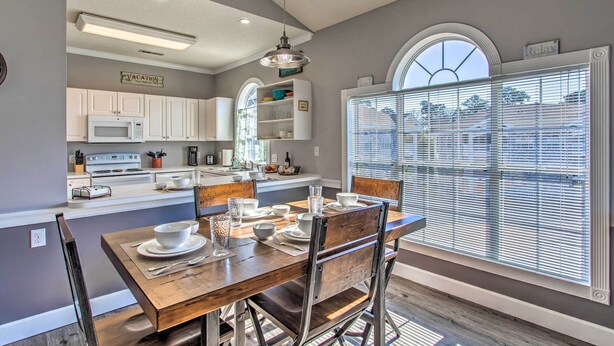 A modern kitchen with white cabinets, a dining table set for four, and a large window with blinds.