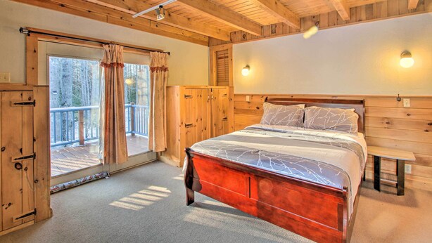 Un dormitorio de cabaña de madera con una cama grande, un puerta corrediza de vidrio a un balcón y paredes de madera.