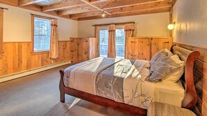 Un dormitorio con paneles de madera, una cama grande, dos ventanas con cortinas y techo de madera.