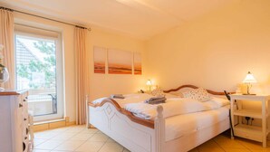 Quarto com cama, mesa de cabeceira, luminária, janela com cortinas e vista para o exterior.
