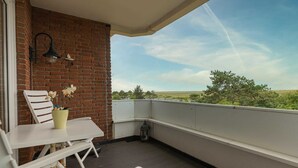 Uma varanda com mesa e cadeiras brancas, um muro de tijolos e vista para o verde.