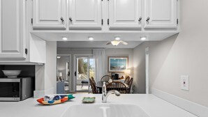 A modern kitchen with white cabinets, a stainless steel microwave, a sink, and a dining area with a table and chairs. - Roomy & Spacious Villa with Great Marsh Views! (Seabrook Island)