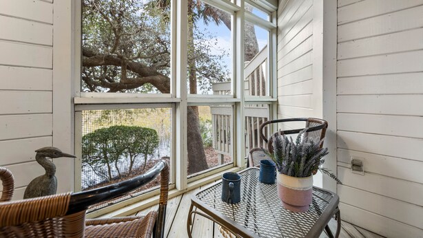 A covered porch with wicker furniture, a potted plant, and a bird perched on a chair. - Roomy & Spacious Villa with Great Marsh Views! (Seabrook Island)