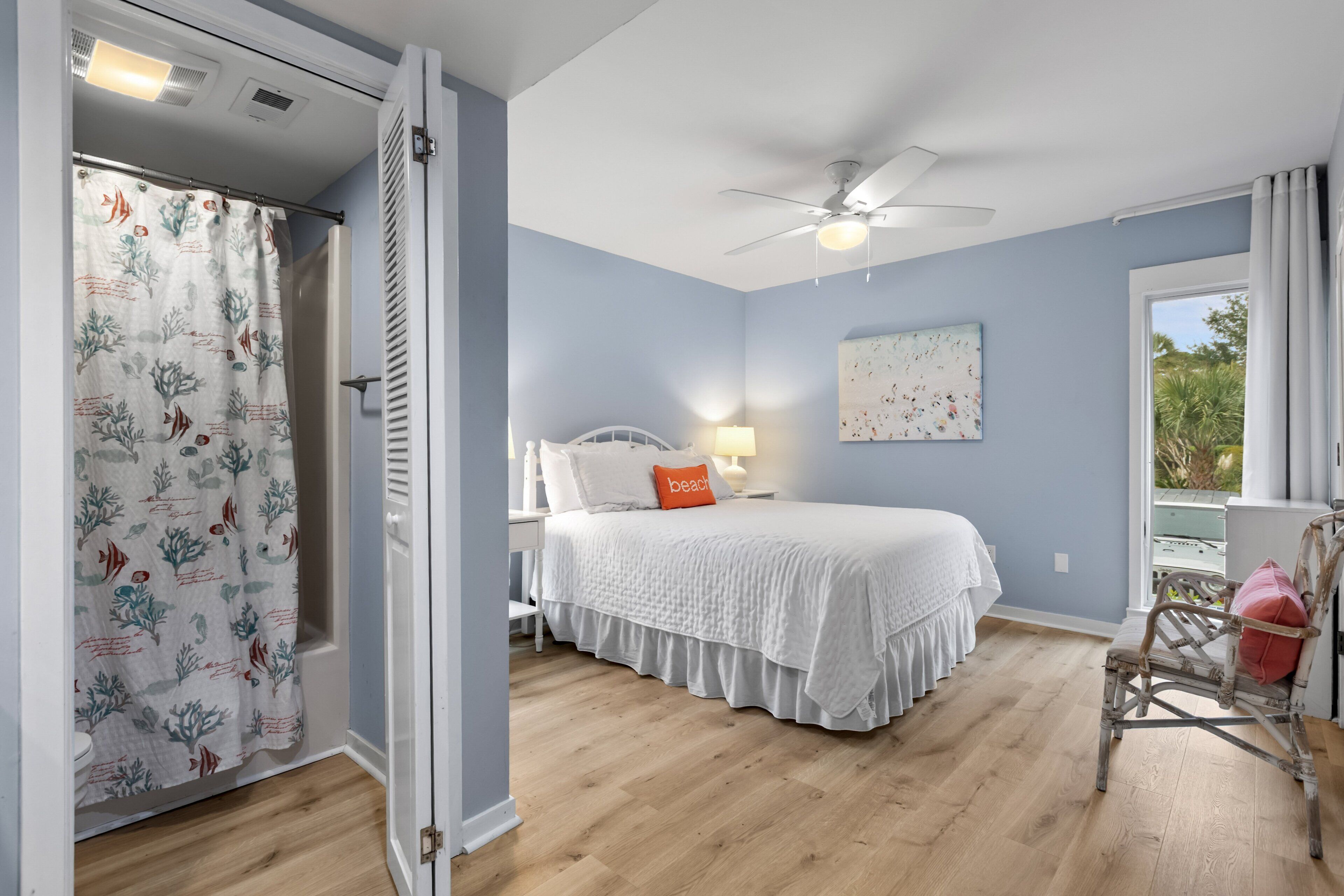 A bedroom with a bed, a nightstand, a chair, a window with curtains, and a ceiling fan.