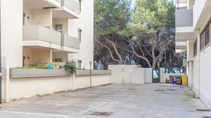 Un patio con piso de concreto, un pequeño jardín con plantas y una reja que da a un estacionamiento.