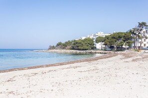 A beach with a sandy shore, a calm sea, and a row of white buildings with trees in the background.