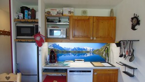 A compact kitchen with a microwave, coffee maker, and a dishwasher. There is a wooden cabinet above the sink and a small trash bin to the right.